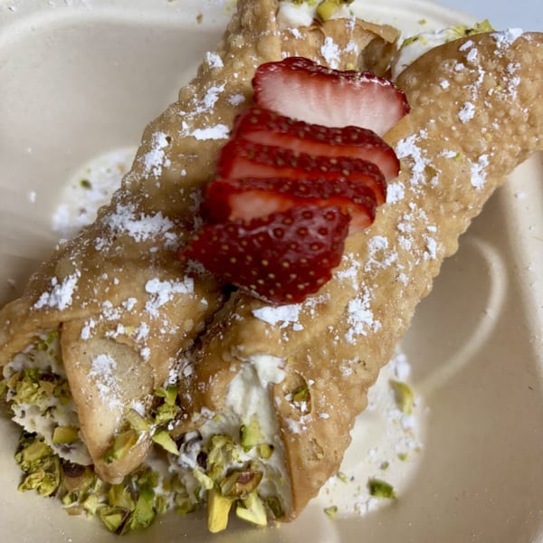 Two cannolis filled with cream, topped with sliced strawberries, pistachios, and powdered sugar.