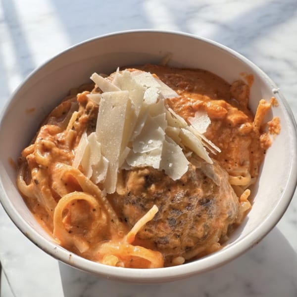 Creamy pasta with a large meatball and shaved Parmesan cheese in a white bowl.