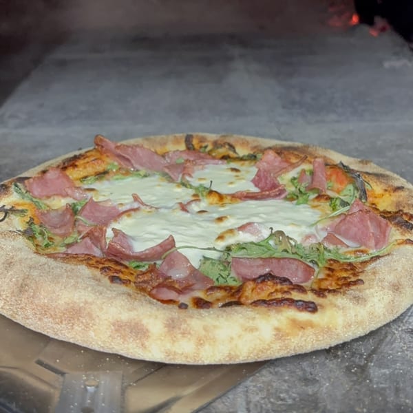 Maeposas pizza with melted mozzarella, arugula, and thinly sliced meat, fresh from the oven.