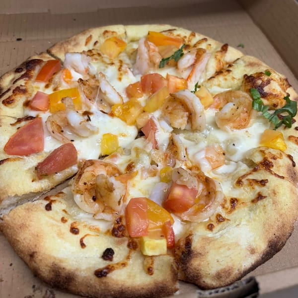 Maeposas shrimp pizza with melted cheese, diced tomatoes, and bell peppers in a cardboard box.