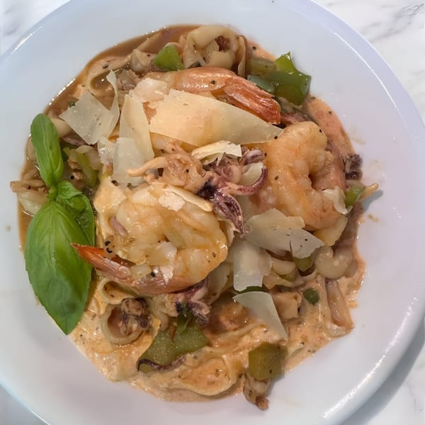 Seafood pasta with shrimp, squid, green peppers, and parmesan cheese, garnished with basil.