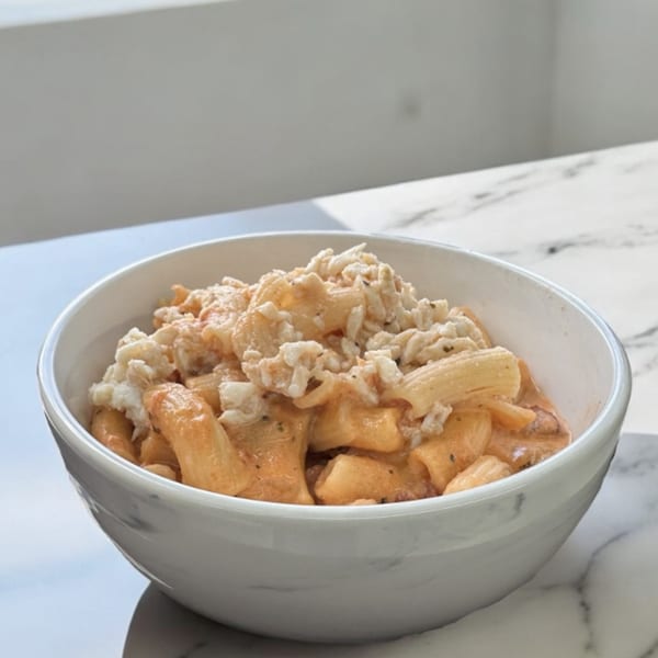 A white bowl filled with creamy pasta topped with shredded white meat on a marble surface.