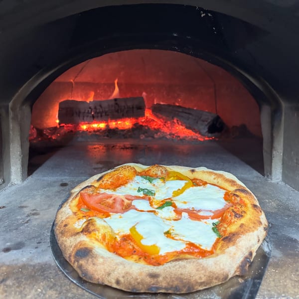 A Maeposas pizza with fresh mozzarella, tomatoes, and basil, cooking in a wood-fired oven.