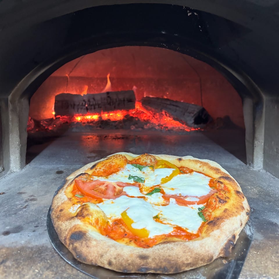 A Maeposas pizza with fresh mozzarella, tomatoes, and basil, cooking in a wood-fired oven.